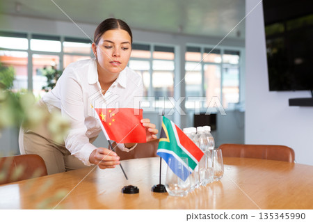Female employee of the delegation sets flags of countries of China and South Africa on the table before start of negotiations 135345990