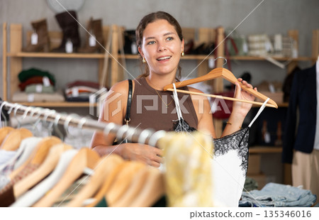 Young woman choosing a top near a hanger Young woman choosing a top near a hanger 135346016
