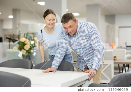Spouses choose dining table desk in furniture store showroom 135346039