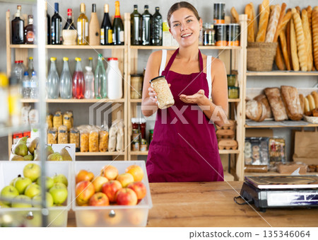 Portrait of friendly girl seller behind a store counter offering to buy canned beans and legumes Portrait of friendly girl seller behind a store counter offering to buy canned beans and legumes 135346064