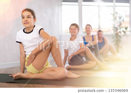 School children and their parents exercising on mats in Lord of the Fishes Pose, or Matsyendrasana during family yoga training in gym fitness center indoors 135346069
