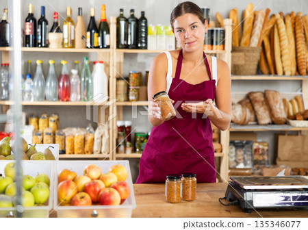 Portrait of friendly girl seller behind a store counter offering to buy canned lentils 135346077