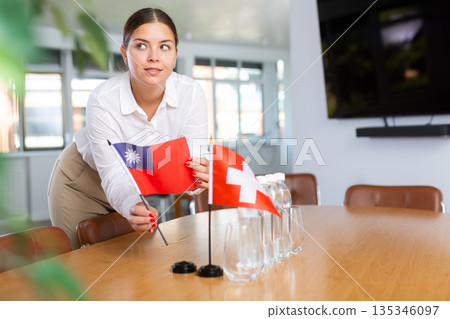 Positive young woman putting little flag of Taiwan on table next to the flag of Switzerland 135346097