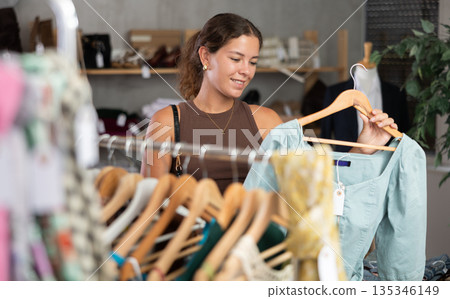 Girl customer choose dress in store, and buyer carefully examines product. 135346149