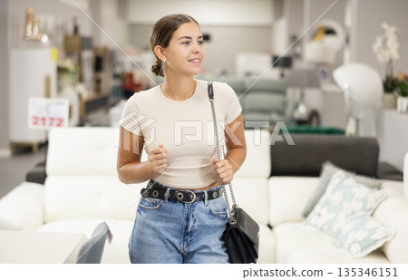 Smiling young girl looking for pieces of furniture in showroom 135346151
