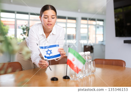 Woman secretary prepares an office for negotiations - she places flags of Iran and Israel table Woman secretary prepares an office for negotiations - she places flags of Iran and Israel table 135346153