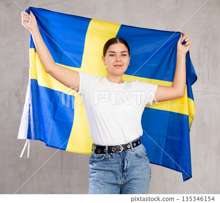 Smiling young woman holding Sweden flag Smiling young woman holding Sweden flag 135346154