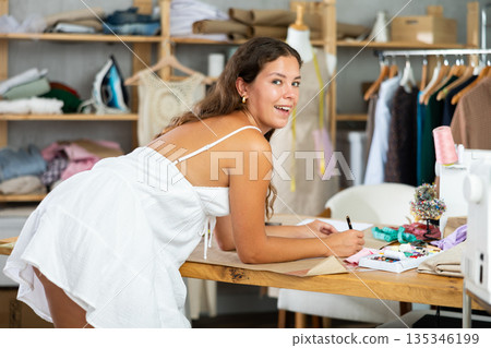 Dressmaker draws a model of clothes on paper in a workshop Dressmaker draws a model of clothes on paper in a workshop 135346199