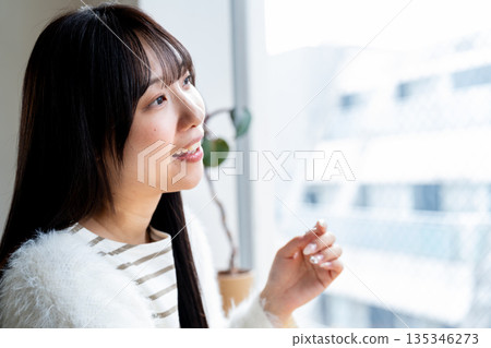 一位微笑、神態放鬆的女子正望著窗外。 一位微笑、神態放鬆的女子正望著窗外。 135346273