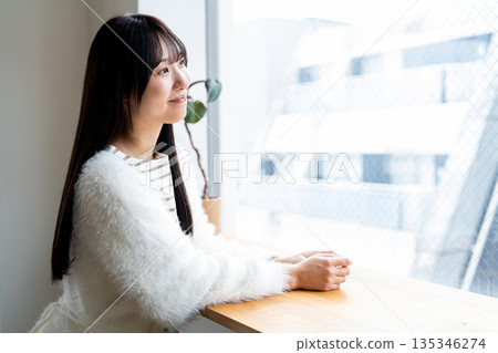 一位微笑、神態放鬆的女子正望著窗外。 一位微笑、神態放鬆的女子正望著窗外。 135346274