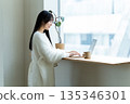 一位微笑的女子在窗邊使用筆記型電腦。 135346301