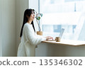 一位微笑的女子在窗邊使用筆記型電腦。 135346302