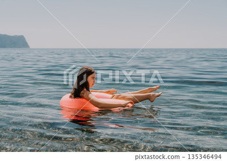 Sea vacation floating young girl relaxes on a pink inflatable ring in calm blue water during summer holiday with copy space Sea vacation floating young girl relaxes on a pink inflatable ring in calm blue water during summer holiday with copy space 135346494