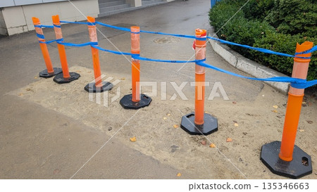 Weathered plastic safety posts with blue rope attachment on wet pavement 135346663