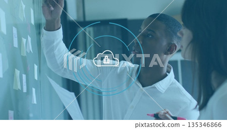 African American man placing sticky note on glass wall in office, with paper, marker, cloud overlay African American man placing sticky note on glass wall in office, with paper, marker, cloud overlay 135346866