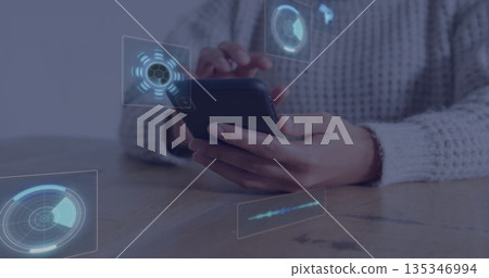 Holding smartphone, woman tapping screen on wooden table inside room, with holographic UI overlays 135346994