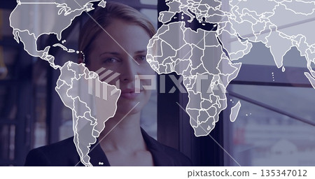 Standing businesswoman surveying skyline at corporate office window panels, with world map overlay Standing businesswoman surveying skyline at corporate office window panels, with world map overlay 135347012