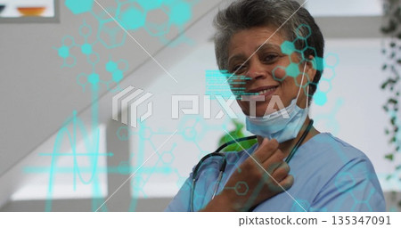 Doctor pulling mask down and smiling in clinic with stethoscope and data overlay, copy space Doctor pulling mask down and smiling in clinic with stethoscope and data overlay, copy space 135347091