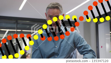 Gesturing man in blue shirt explaining DNA double helix graphic in office, with computer monitor Gesturing man in blue shirt explaining DNA double helix graphic in office, with computer monitor 135347120