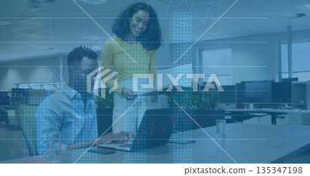 Collaborating colleagues reviewing printed report and analyzing charts at open office, with laptop 135347198