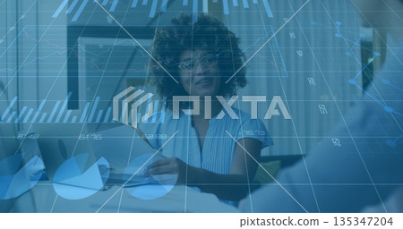 Discussing executive holding charts, speaking to colleague at office desk with monitor overlay 135347204