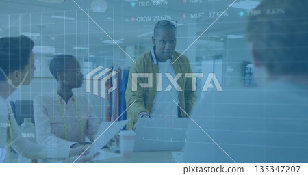 Black man presenting in open-plan office, with laptop, documents, measuring tape and clothing rack 135347207