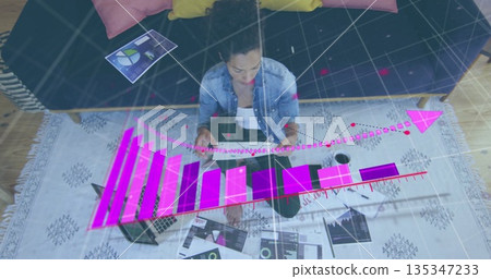 Analyzing woman wearing denim shirt, reviewing data at home, with tablet and 3D graphs 135347233