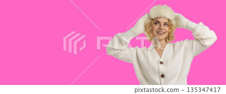 Woman wearing a fluffy hat smiles against a pink backdrop Woman wearing a fluffy hat smiles against a pink backdrop 135347417