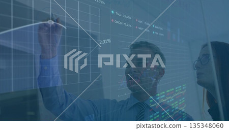 Colleagues wearing business attire annotating financial charts on office glass board, using marker Colleagues wearing business attire annotating financial charts on office glass board, using marker 135348060
