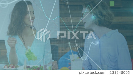 Two colleagues sharing fresh salad and chatting in office break area, with fruit plate, chopsticks 135348095