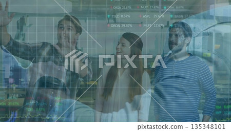Three business professionals analyzing data on transparent screen in office, stock tickers overlay 135348101