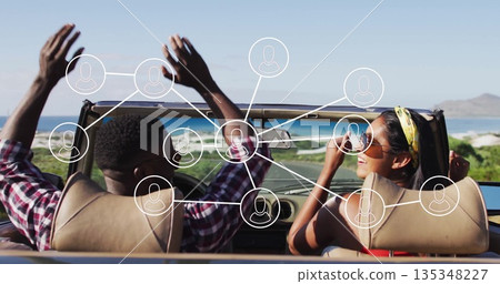Driving couple waving arms and smiling in convertible car on coastal highway with network overlay Driving couple waving arms and smiling in convertible car on coastal highway with network overlay 135348227
