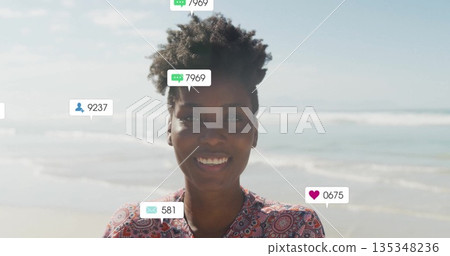 Standing woman wearing red and white top viewing floating social media icons at beach shoreline 135348236