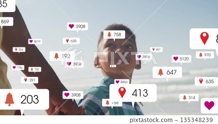 Walking father in yellow top son in green shirt holding hands on beach, floating notification icons 135348239