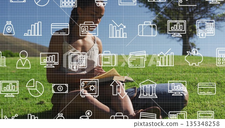 Reading woman sitting cross-legged on grass at lakeside park, with book and financial icons overlay 135348258
