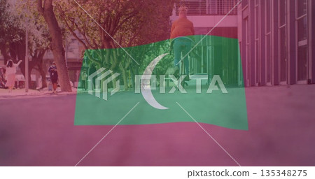 Riding cyclist wearing orange jacket along tree-lined pathway by glass facade, with flag overlay 135348275