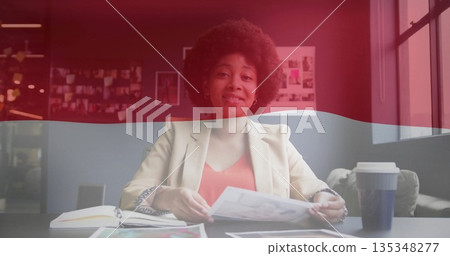Holding printed picture designer in cream blazer at office desk, with coffee cup notebook pinboard Holding printed picture designer in cream blazer at office desk, with coffee cup notebook pinboard 135348277