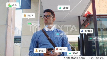Checking Hispanic man holding smartphone, viewing notification icons at office entrance, with bag 135348392