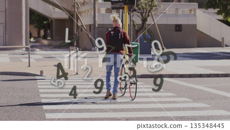 Man wearing red shirt pushing bicycle across zebra crosswalk at city intersection, with backpack 135348445