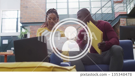 Reviewing printed charts coworkers wearing shirts on blue sofa in lounge, with mug yellow folders Reviewing printed charts coworkers wearing shirts on blue sofa in lounge, with mug yellow folders 135348478