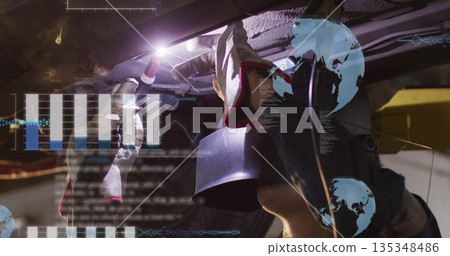 Welding helmeted mechanic using torch under raised vehicle chassis at workshop, with AR overlays 135348486