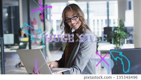Holding laptop, woman wearing glasses and grey blazer sharing work in open office, with glass wall 135348496