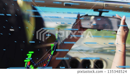 Holding tablet, Indian woman analyzing AR data over wing in cockpit, with numeric readouts 135348524