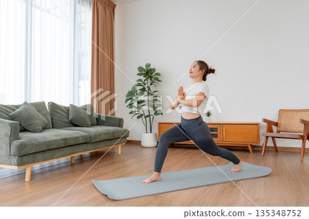 Happy young Asian woman practicing yoga and shoulder stretching  in living room at home 135348752