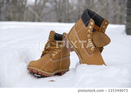 Iconic tan work boots with yellow laces stand in fresh winter snow Iconic tan work boots with yellow laces stand in fresh winter snow 135349073