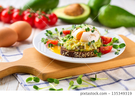 Avocado toast with poached egg over rye bread toast with mashed avocado spread. Healthy breakfast or lunch food. Avocado toast with poached egg over rye bread toast with mashed avocado spread. Healthy breakfast or lunch food. 135349319
