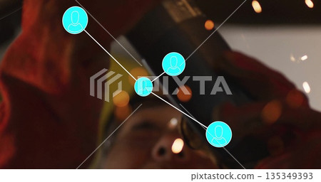 Reaching worker wearing yellow hard hat and red jacket gripping pipe in workshop, with tool sparks Reaching worker wearing yellow hard hat and red jacket gripping pipe in workshop, with tool sparks 135349393