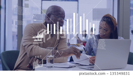 Senior mentor and mentee reviewing documents and holding pen at office desk, with silver laptop Senior mentor and mentee reviewing documents and holding pen at office desk, with silver laptop 135349831