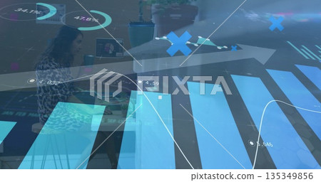 Woman wearing patterned blouse analyzing data graphs at desk, with monitor and potted plant 135349856