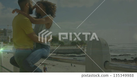 Leaning couple embracing on seaside promenade metal railing, overlooking beach ocean waves Leaning couple embracing on seaside promenade metal railing, overlooking beach ocean waves 135349988
